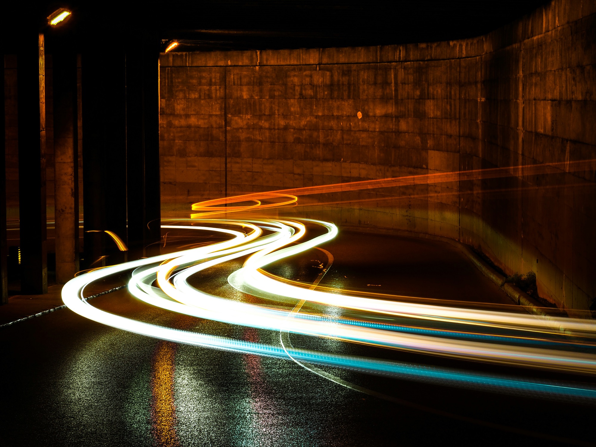 Long-exposure light trails sweeping along a curving road through an underpass at night