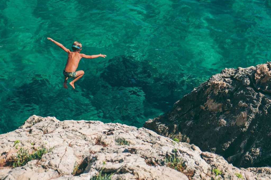 boy jumping into ocean from rocks