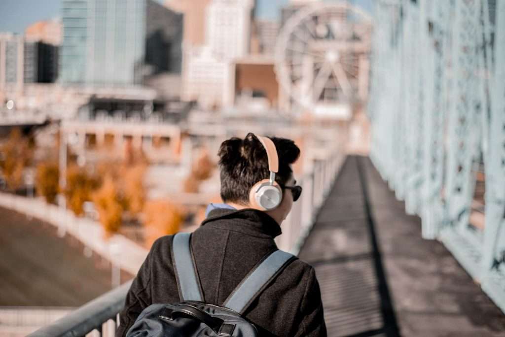 man listening to headphones walking across a bridge