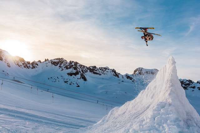 Up in the snowy mountain ranges a skiier does tricks mid jump after going up a snow ramp. Photo used for marketing outsourcing blog.